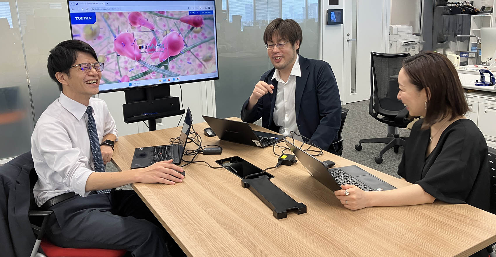 ノートパソコンを広げた三人の社員がテーブルに集まり談笑している様子