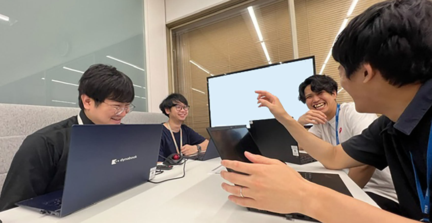 男性社員4名がノートパソコンを広げながら笑顔で談笑している様子
