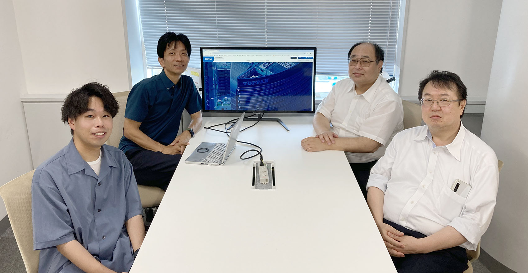 男性社員4名が正面を向いて並んで笑顔をむける様子