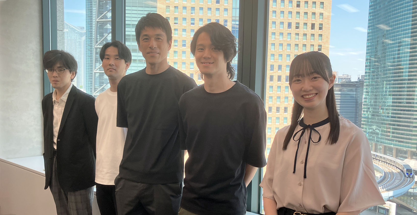 男性社員4名と女性社員1名が正面を向いて並んで笑顔をむける様子