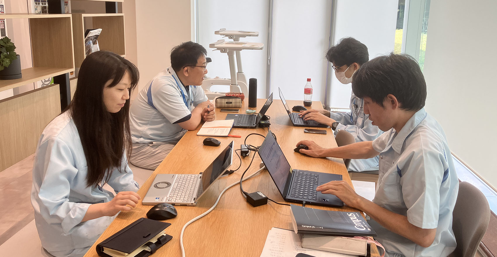 男性社員3名と女性社員1名がノートパソコンを開いて仕事をしている様子