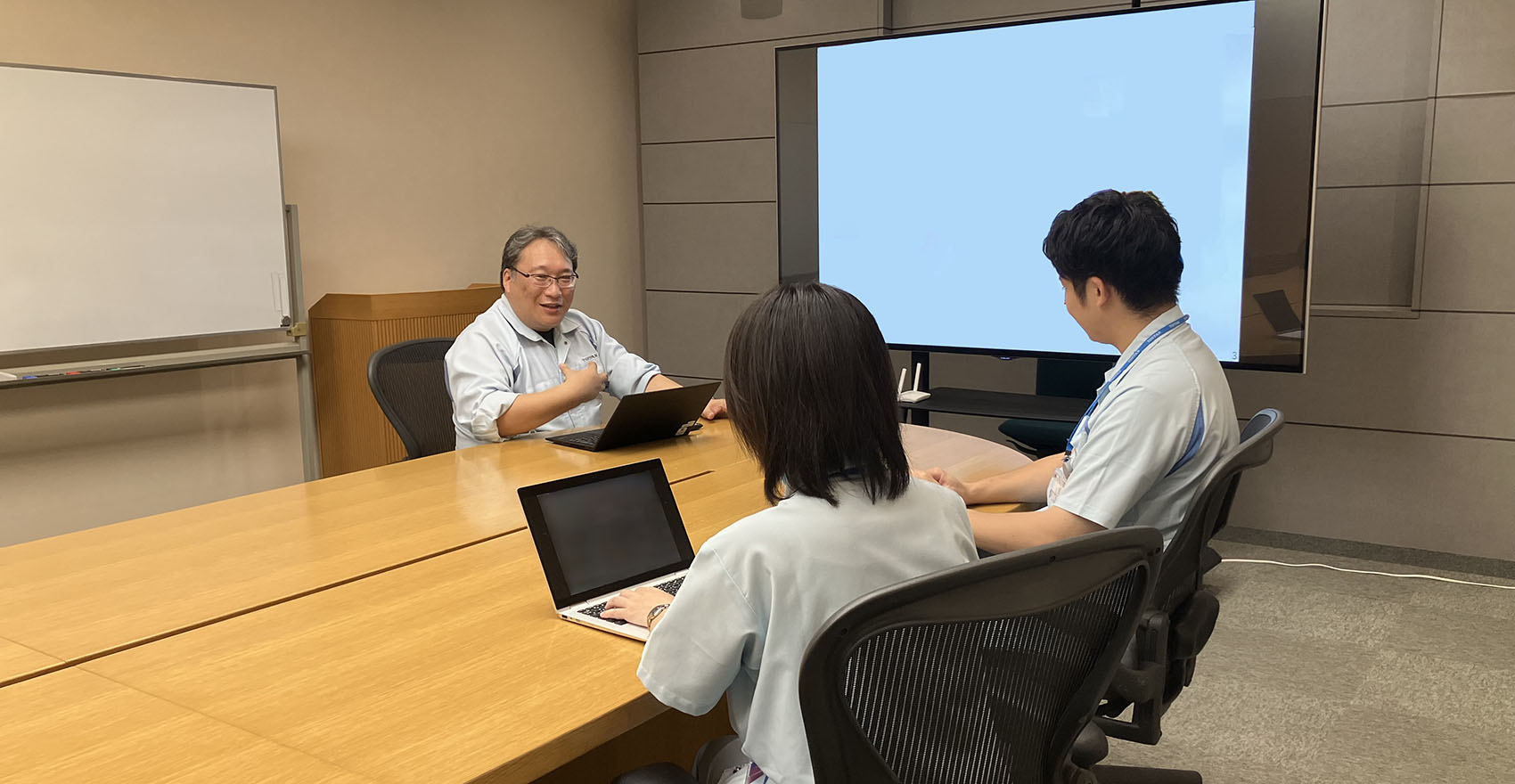 社員3名がノートパソコンとプロジェクターを使いながら打ち合わせを行う様子