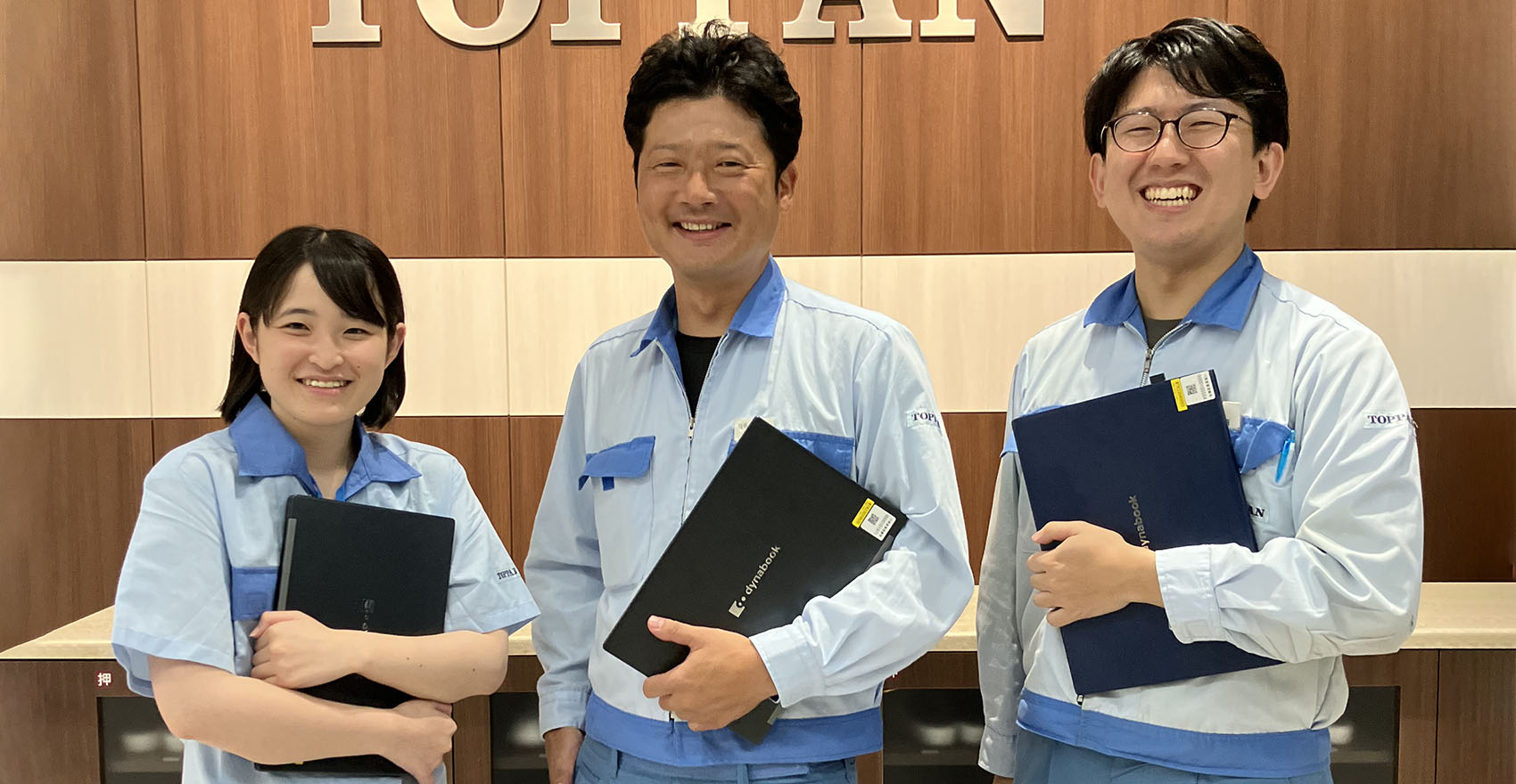 男性社員2名と女性社員1名が正面を向いて並んで笑顔をむける様子